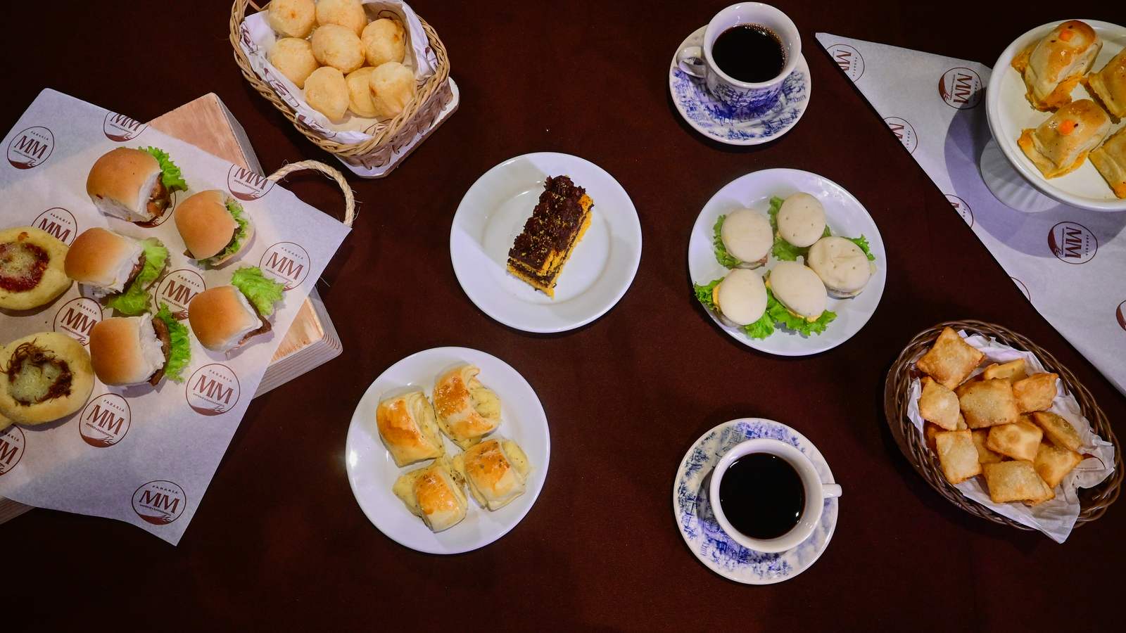 Mesa de festa montada com salgados, mini sanduíches e bolo da Padaria MM